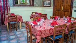Uma área de refeições com uma grande mesa de madeira posta para uma refeição, rodeada por cadeiras de madeira.