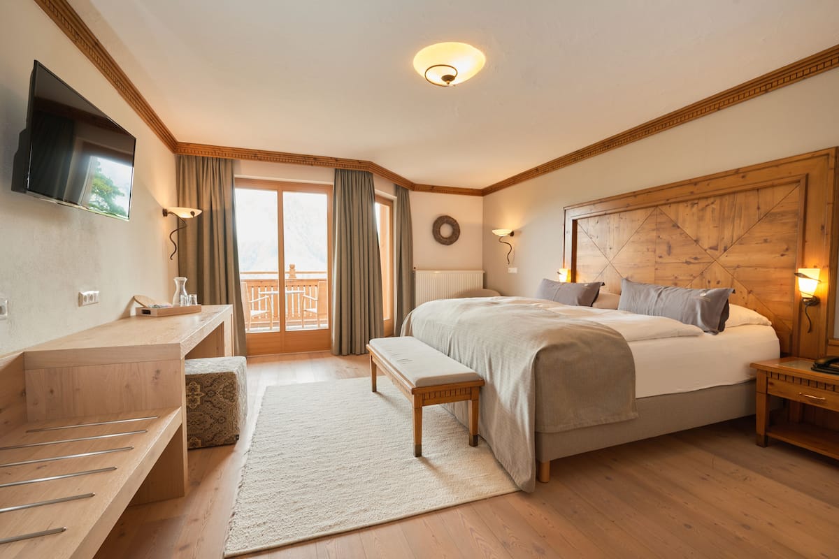 Une chambre d’hôtel avec un lit, des tables de chevet, une télévision, une fenêtre avec des rideaux, une tête de lit en bois et une vue sur l’extérieur.