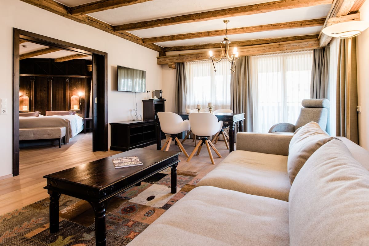 Un salon moderne avec un canapé, une table basse et un coin repas avec des chaises. Le plafond est en bois et il y a un lustre.