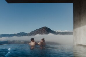Ein Paar in einer heißen Quelle, im Hintergrund ein Berg mit verschneiten Gipfeln.