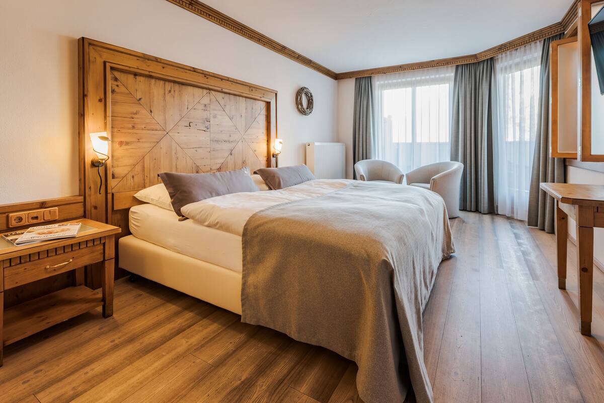 Une chambre d’hôtel avec un lit en bois, un bureau avec une lampe, une chaise et un téléviseur posé sur un meuble en bois.