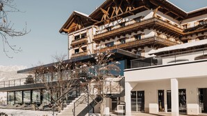 Ein mehrstöckiges Gebäude mit hölzernen Balkonen, einer Glasfassade und einem Skiabhang im Hintergrund.