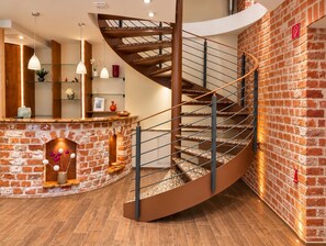 A spiral staircase with a brick wall and wooden floor, leading to an upper level.