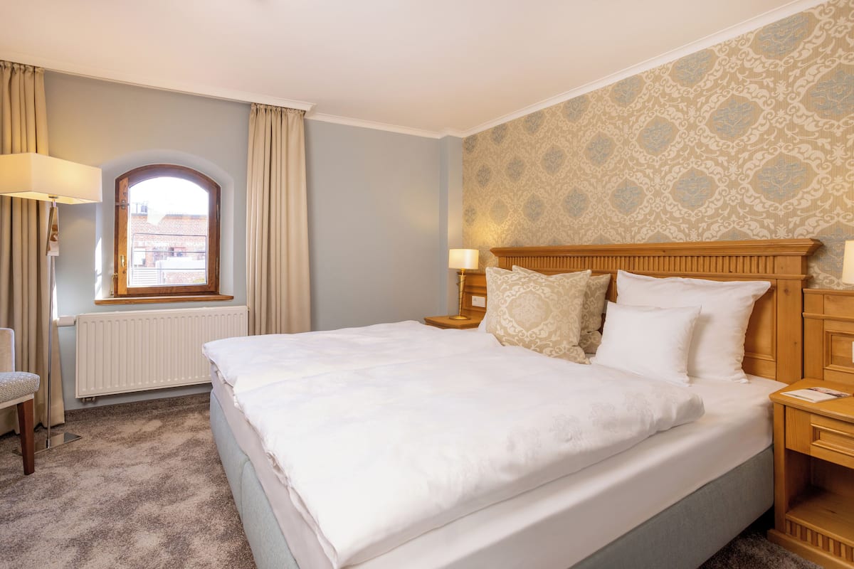 A hotel room with a large bed, a chair, a window, and a radiator.