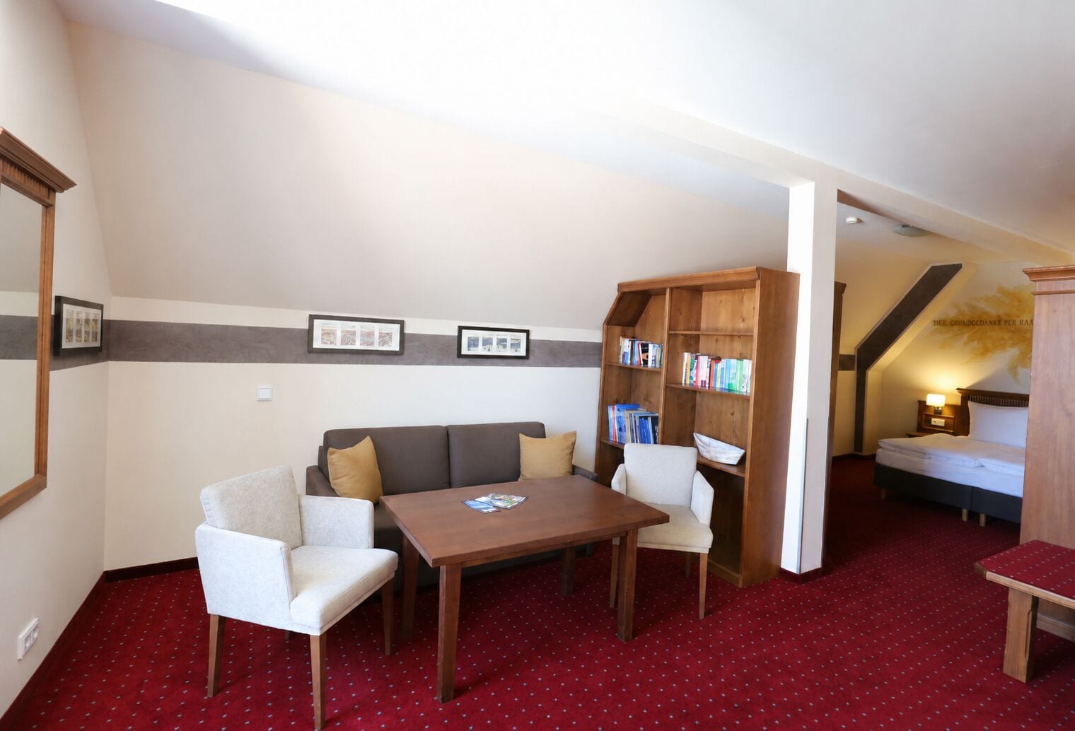 Una habitación con sofá, dos sillones, una mesa, estantería, cama y alfombra roja.