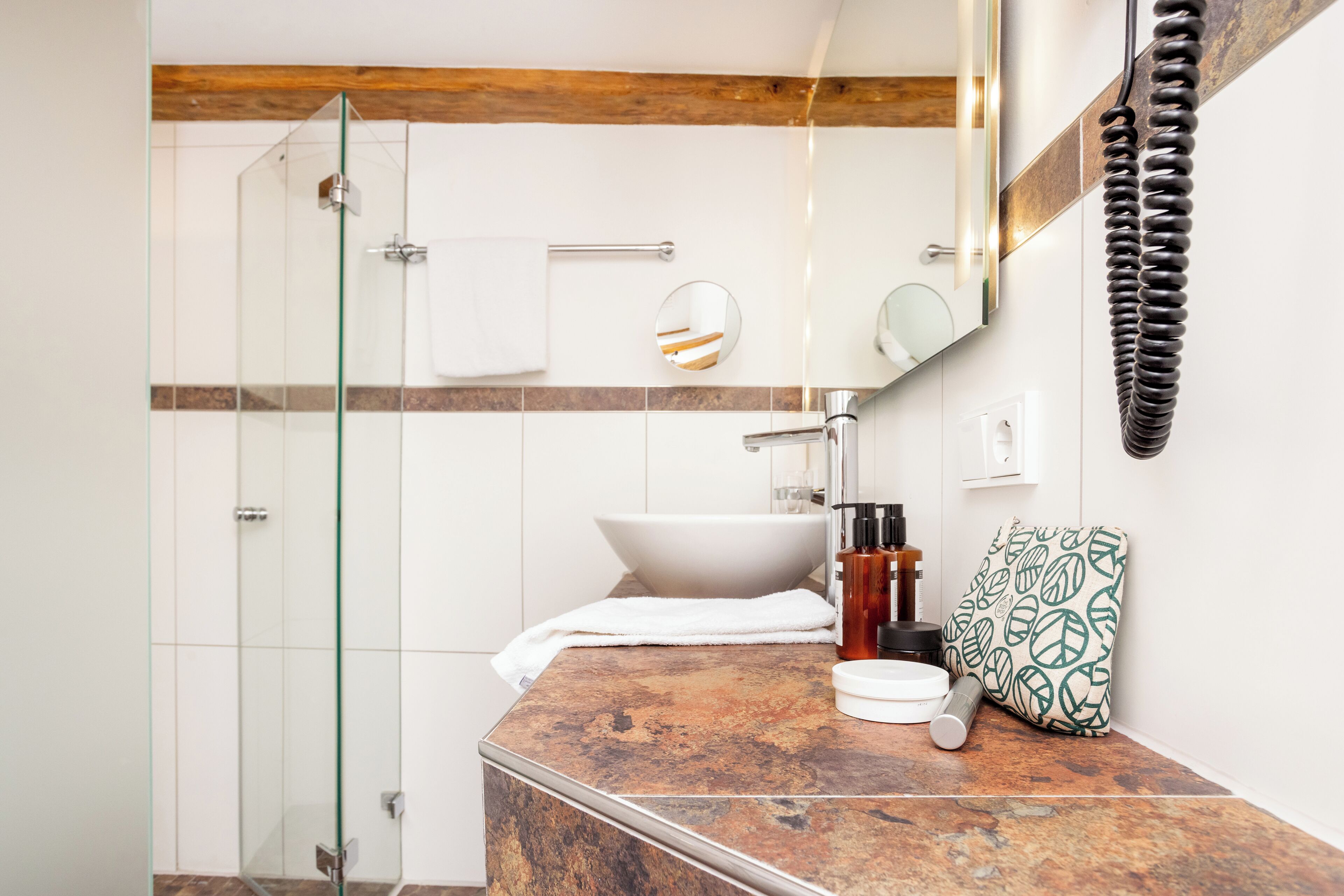 A bathroom with a glass shower enclosure, a white sink, a mirror, and a towel.