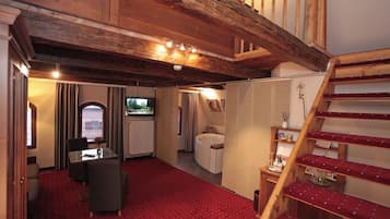 Una camera d'albergo con tappeto rosso, travi in legno a soffitto, un'area pranzo con tavolo e sedie, un bagno con vasca e una scala con gradini rossi.