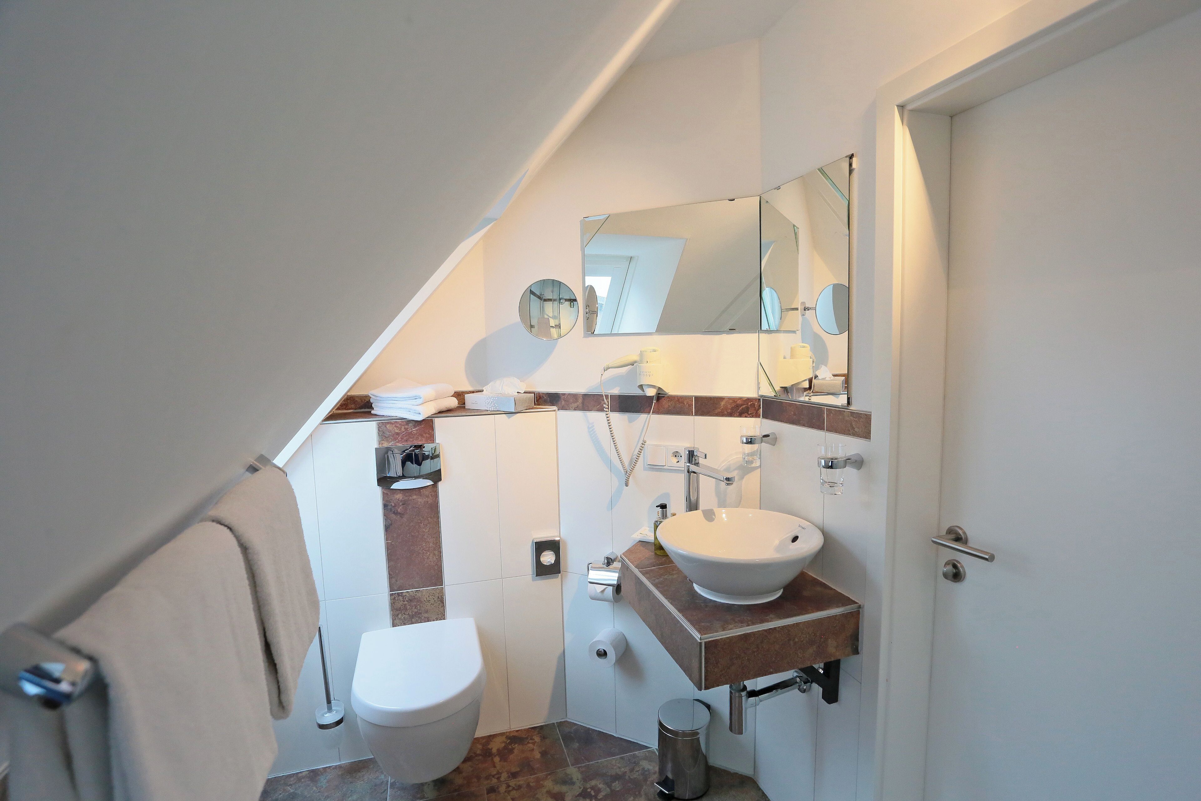 Un baño moderno con inodoro blanco, lavamanos, espejo y toallero.