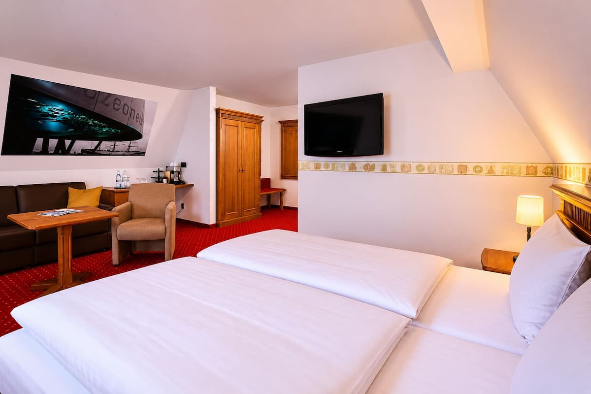 A hotel room with a bed, a TV, a desk with a chair, a wardrobe, and a red carpet.