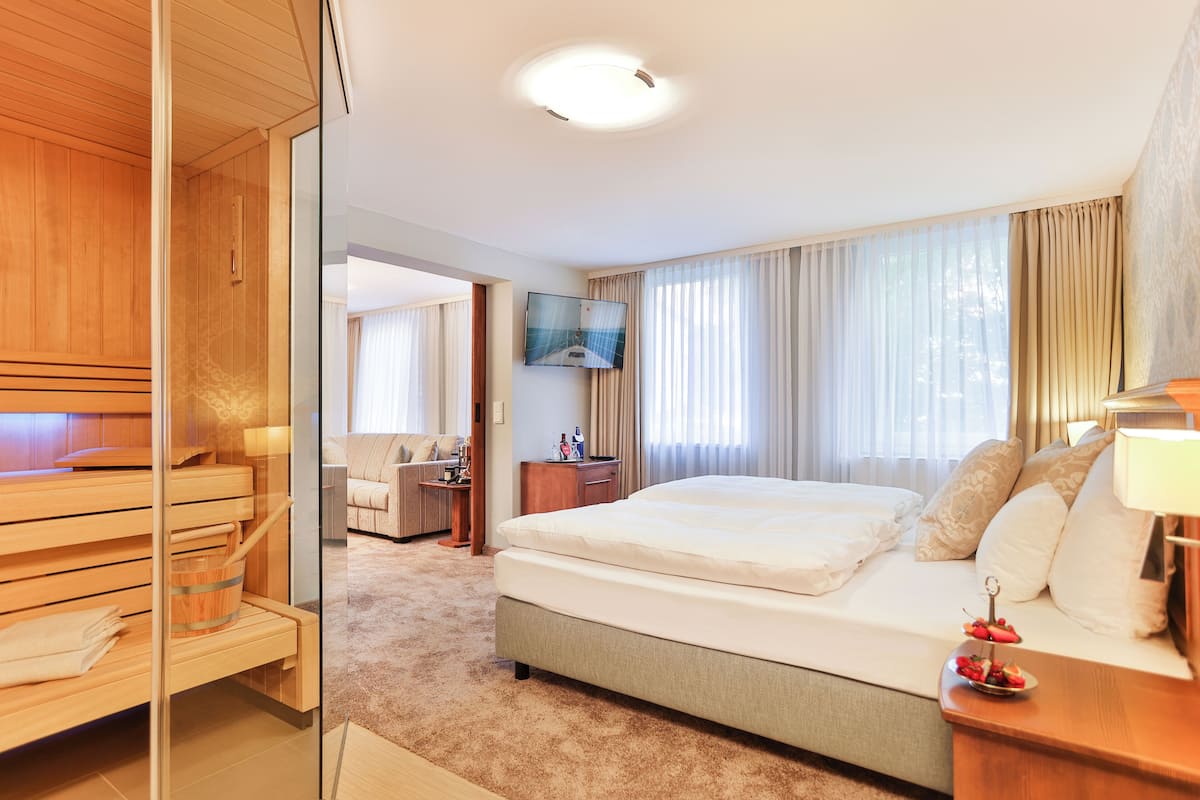 A hotel room with a bed, a desk, a television, and a sauna area.