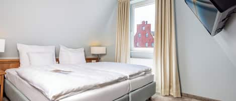 Habitación de hotel con cama, televisión montada en la pared, ventana con cortinas y vista a un edificio.