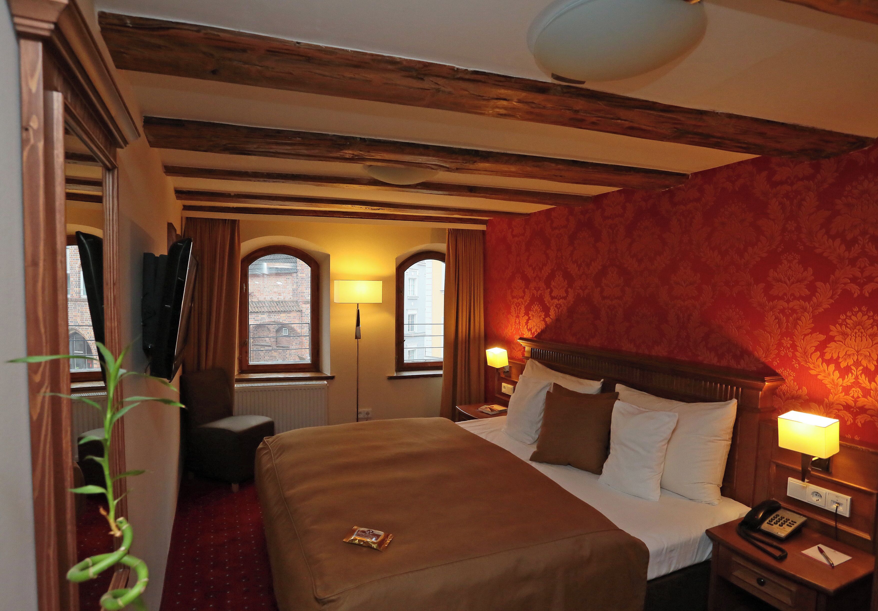 Une chambre d’hôtel avec un lit, deux lampes de chevet, une chaise, un bureau et une fenêtre avec des rideaux.