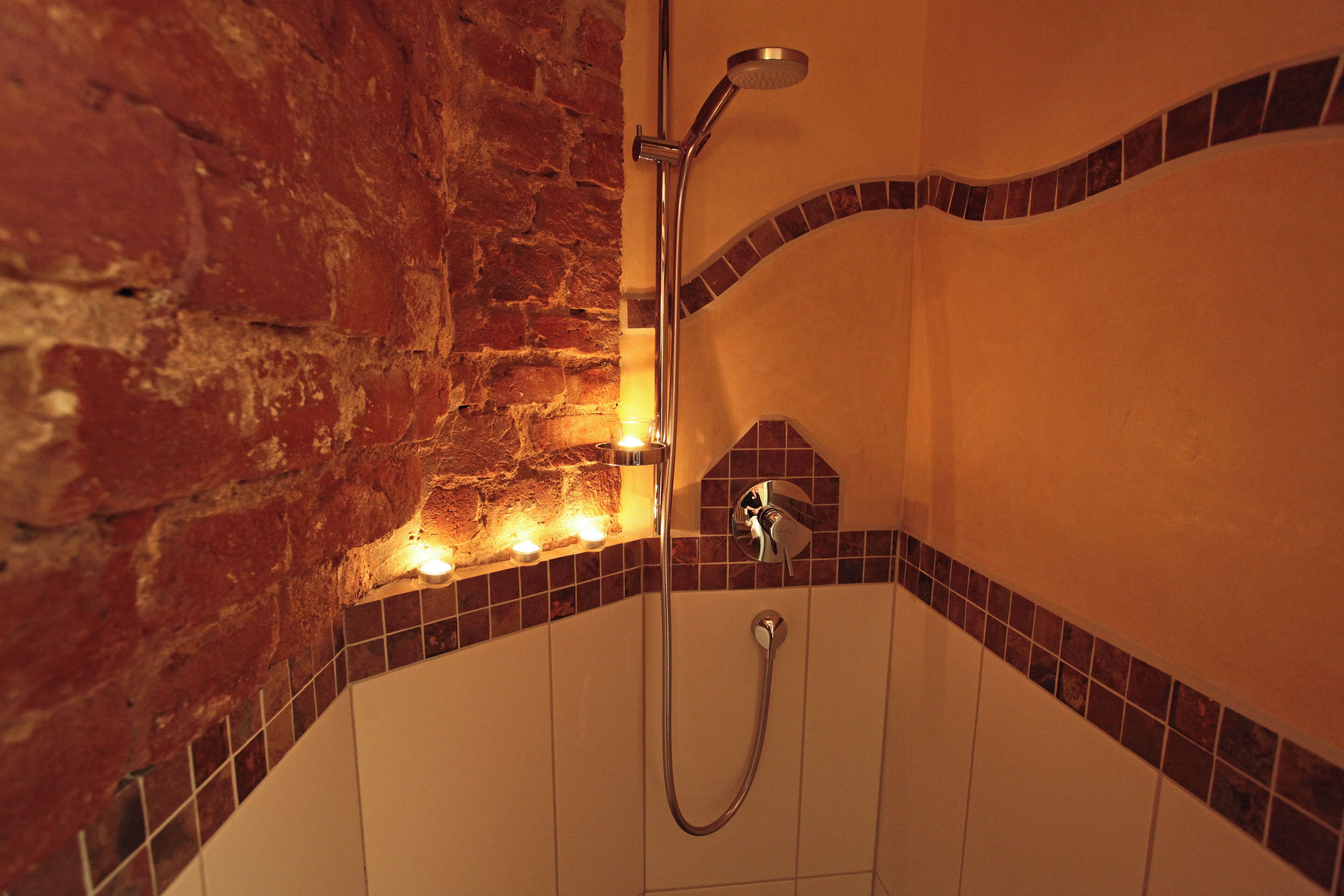 A shower with a chrome fixture, a tiled wall, and a brick wall.