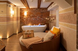A spa room with a brick wall, a bathtub, and a seating area with a towel and a bag.