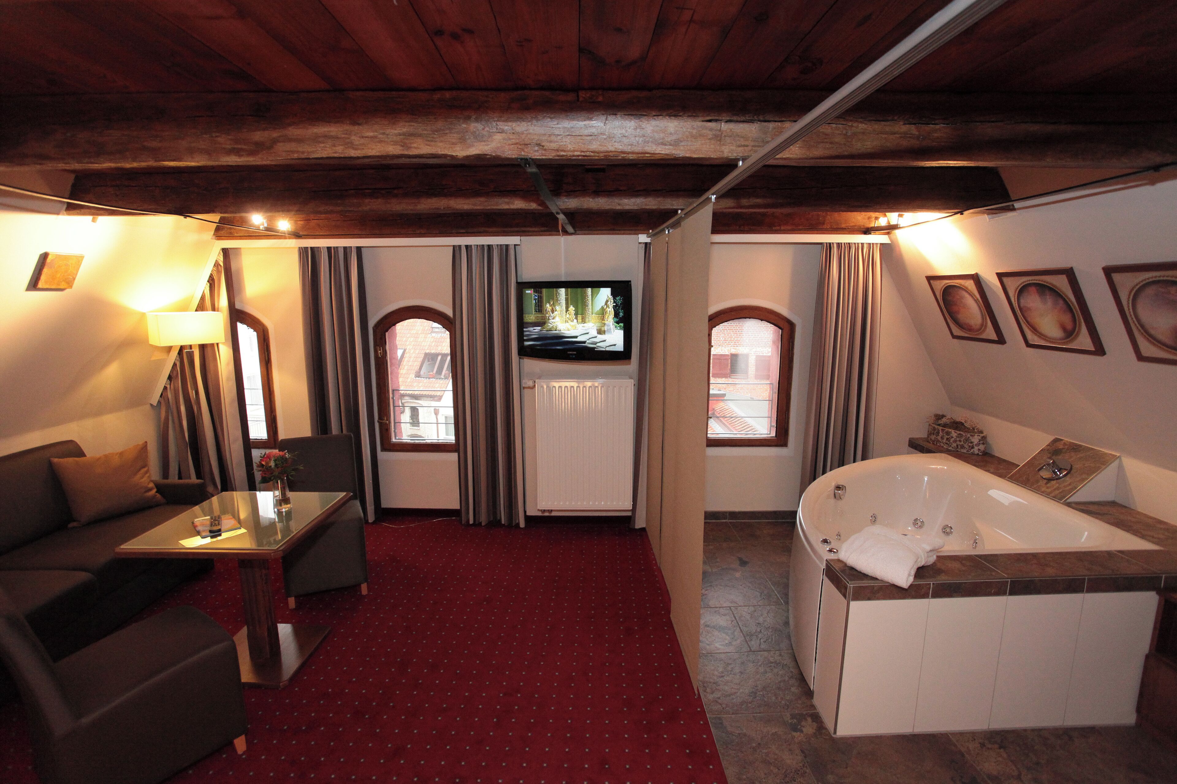Une pièce avec un tapis rouge, un canapé, une télévision, une baignoire et une fenêtre avec des rideaux.