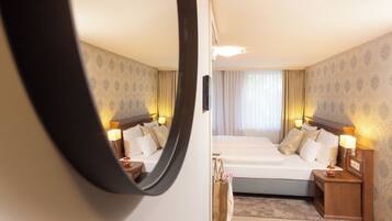 A hotel room with a large bed, bedside tables with lamps, a mirror, and a view of the outside through a window with curtains.