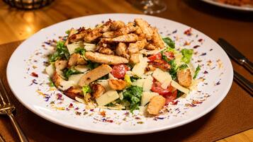A plate of food with grilled chicken, cheese, and vegetables on a white plate with colorful specks.