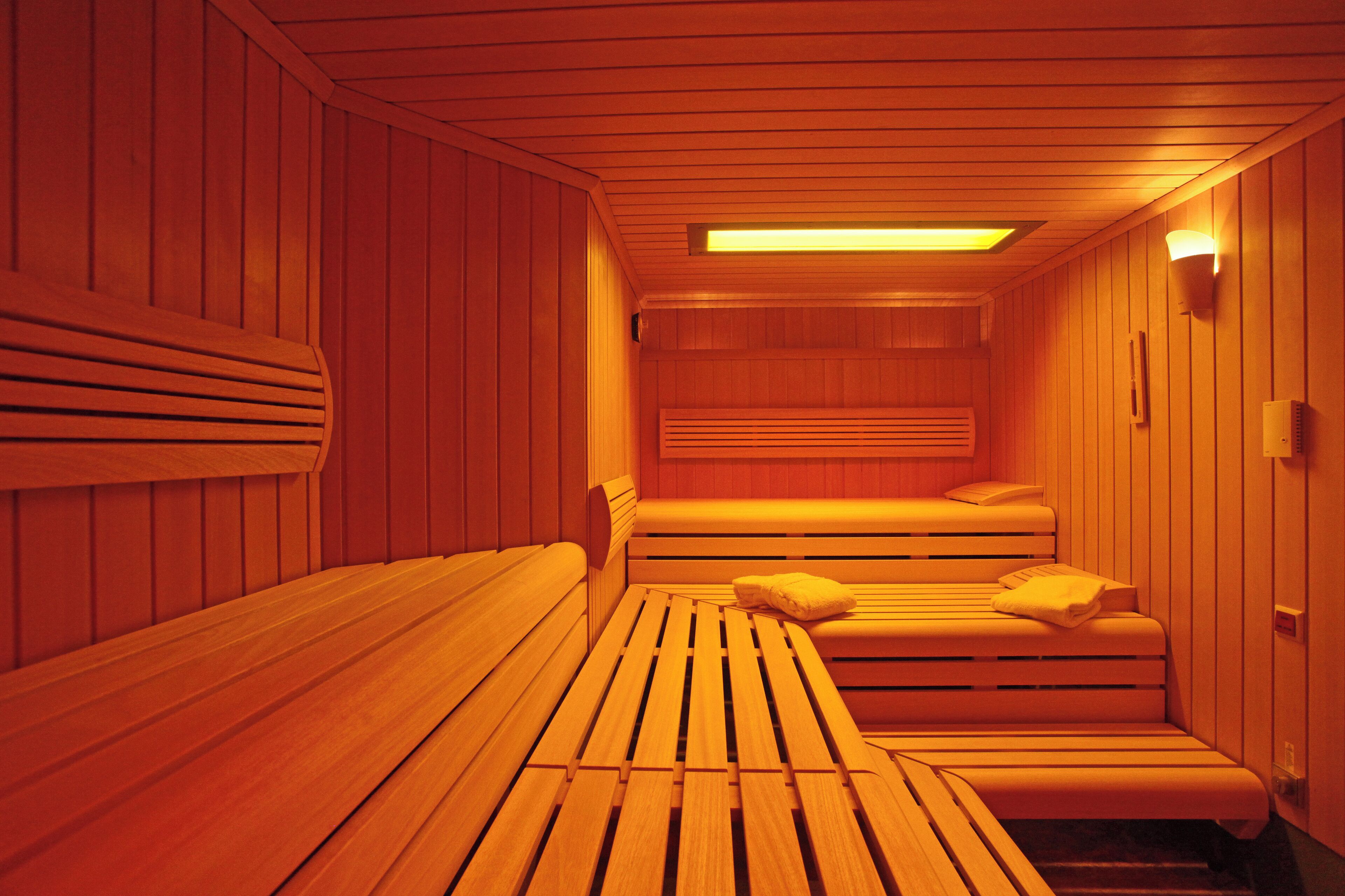 A sauna with wooden benches and benches, a bench with a pillow, and a wall-mounted light fixture.
