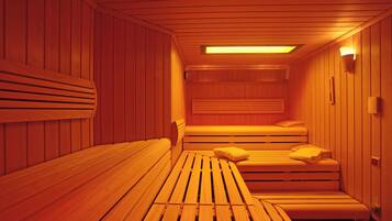 A sauna with wooden benches and benches, a bench with a pillow, and a wall-mounted light fixture.