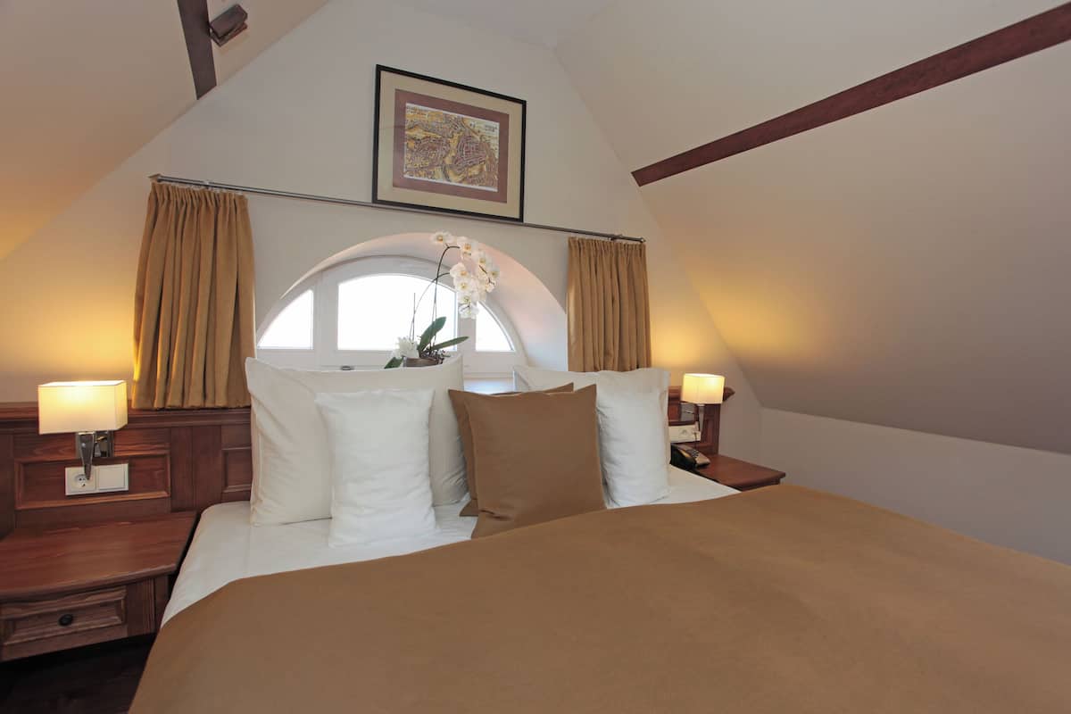 A hotel room with a large bed, two bedside tables, a window with curtains, a framed picture on the wall, and a lamp on each bedside table.