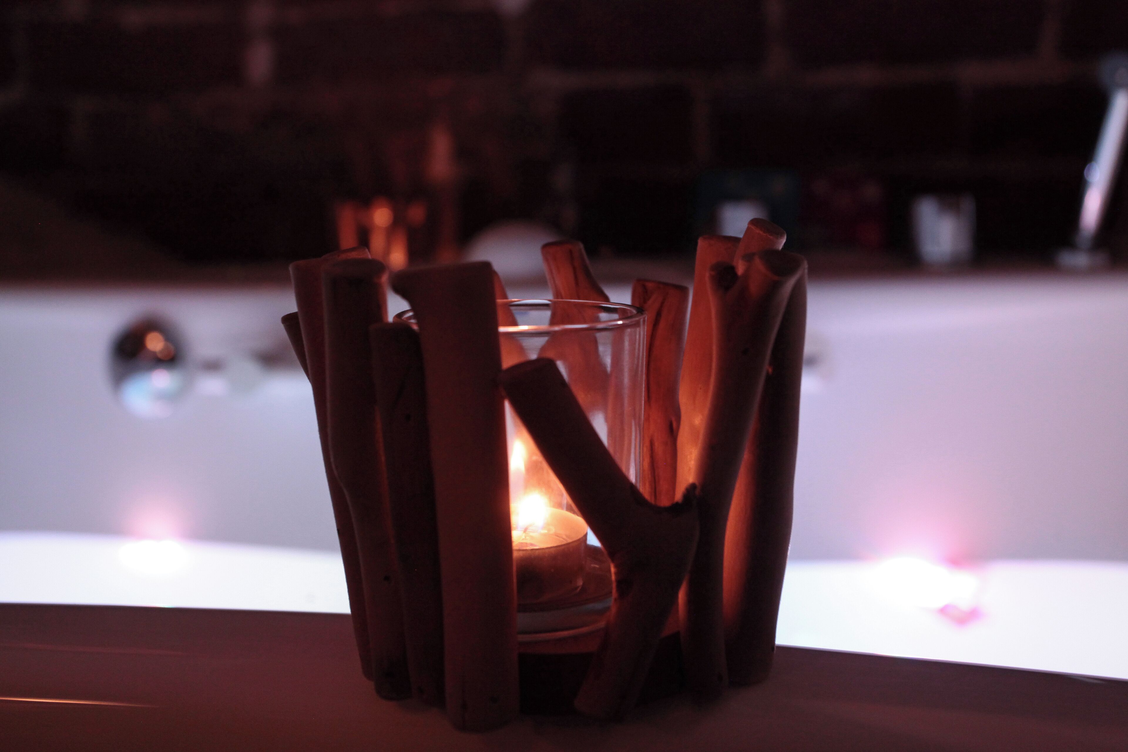 A candle in a glass holder surrounded by wooden sticks.
