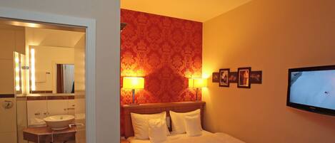 Habitación de hotel con una cama, una mesita de noche, un televisor y un baño visible a través de una puerta abierta.