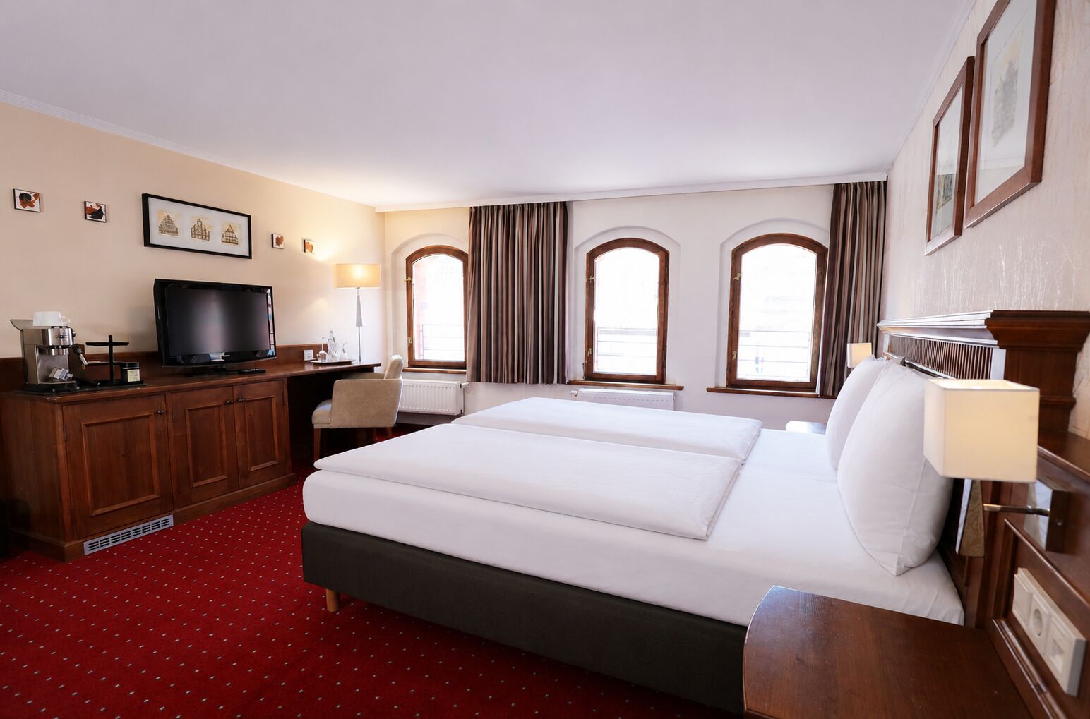 A hotel room with a bed, a desk with a television, a coffee machine, and a chair.