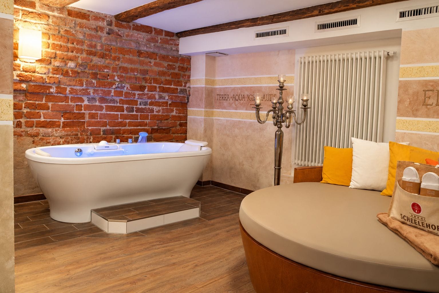 A bathroom with a freestanding bathtub, a wooden floor, a radiator, and a wall with a brick pattern.