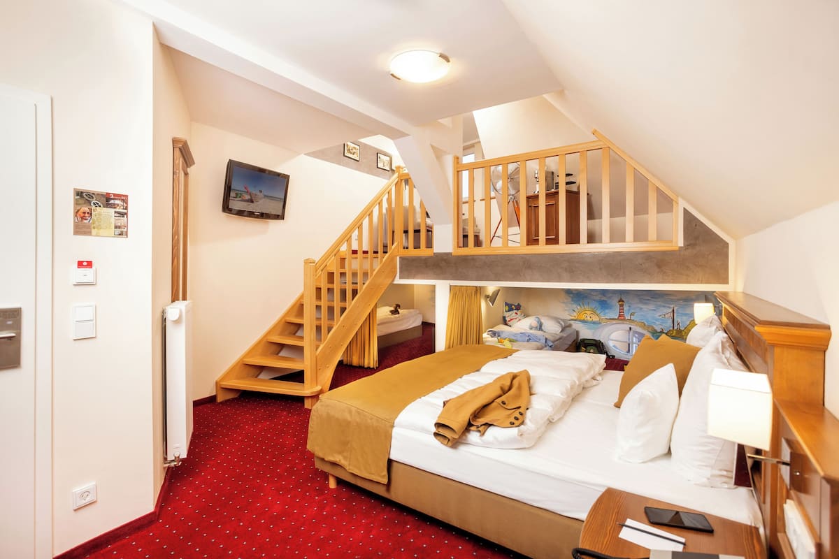 A hotel room with a bunk bed, a wooden staircase, a red carpet, and a painting on the wall.