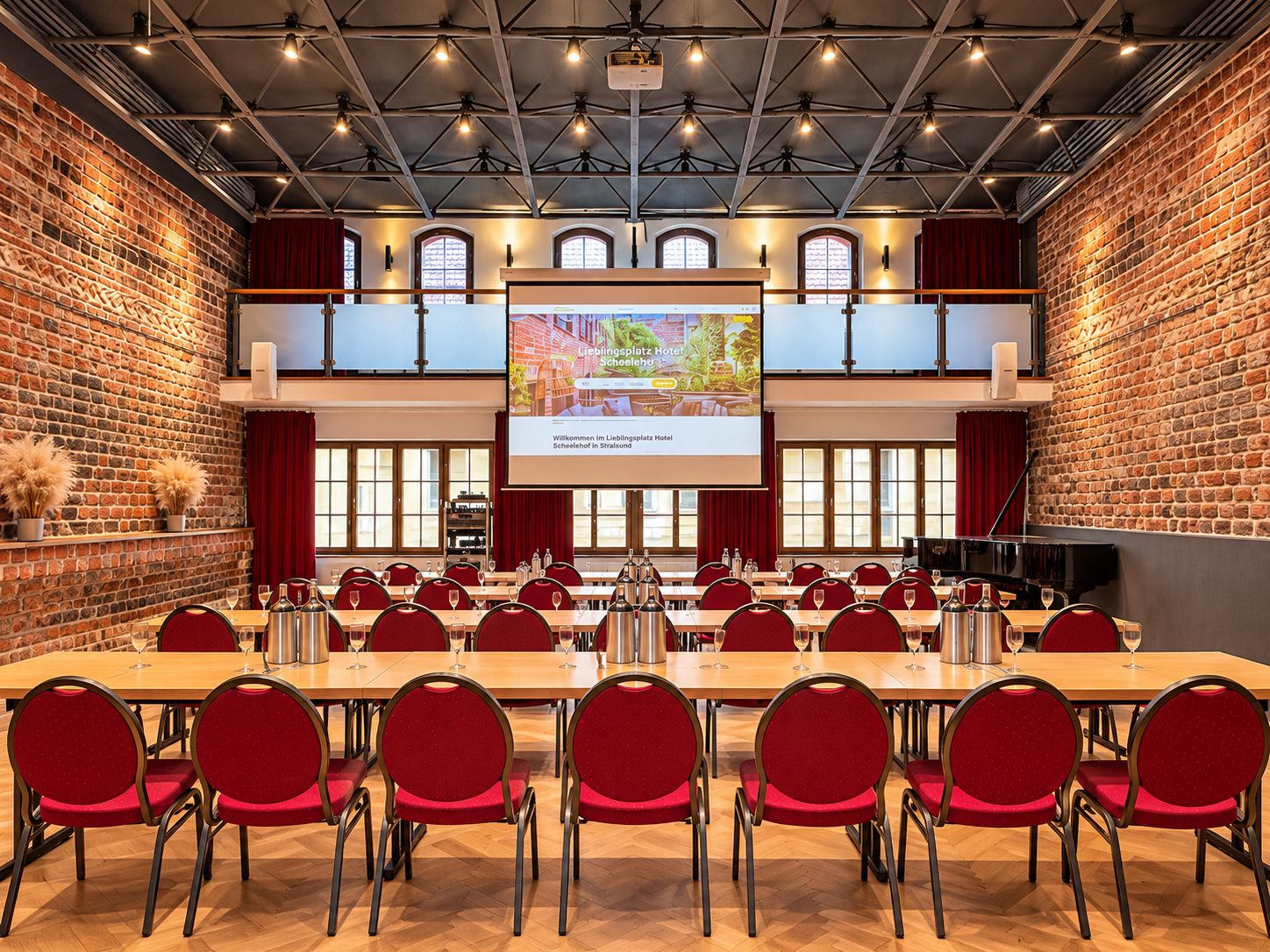 Ein Konferenzraum mit mehreren Tischen und Stühlen, einem großen Bildschirm mit einer Willkommensbotschaft und Ziegelwänden.