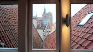 Vista a través de una ventana que muestra un edificio con tejado de tejas, una puerta y un marco de ventana.