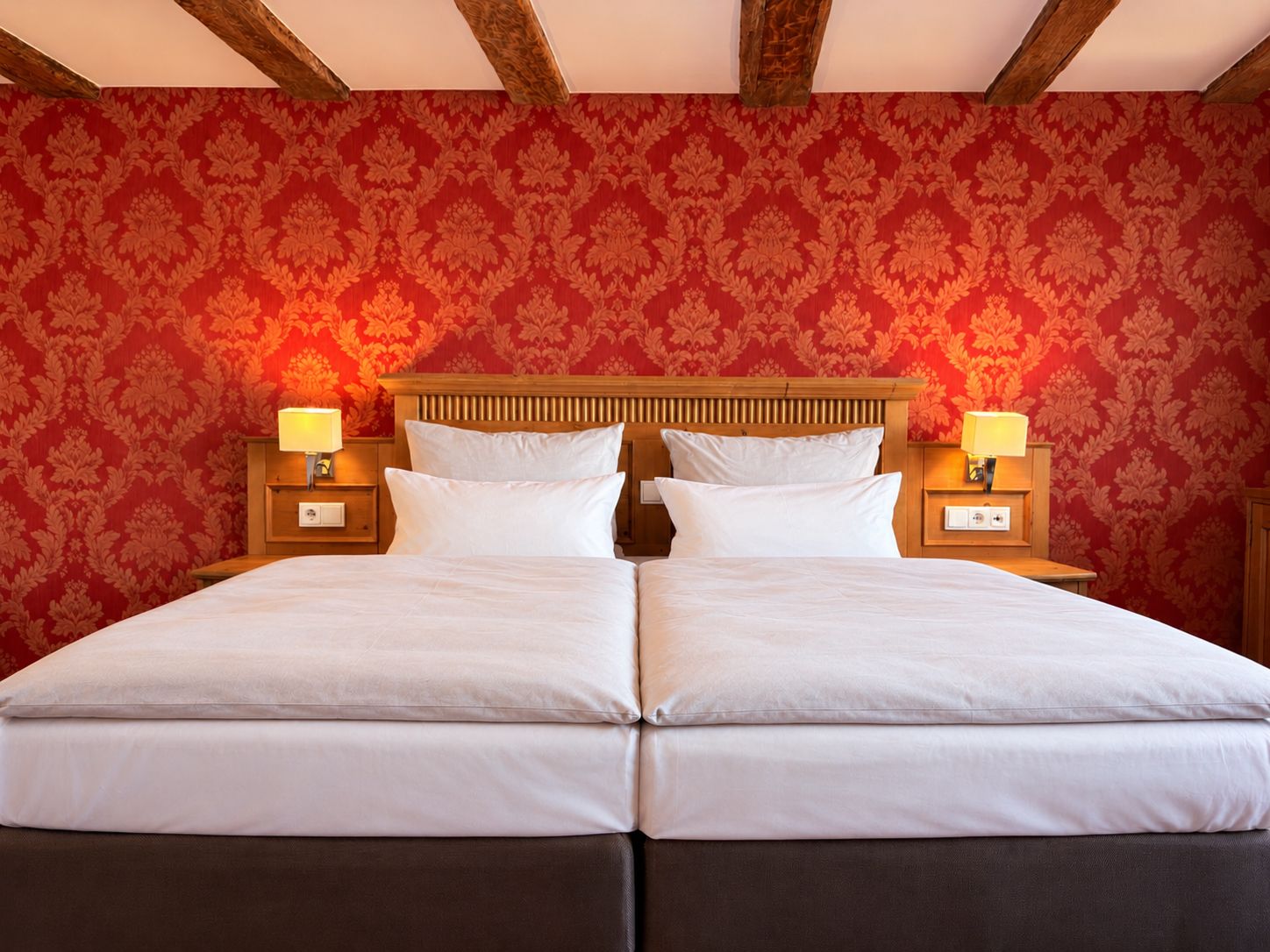 A double bed with a wooden headboard, two bedside tables with lamps, and red patterned wallpaper.