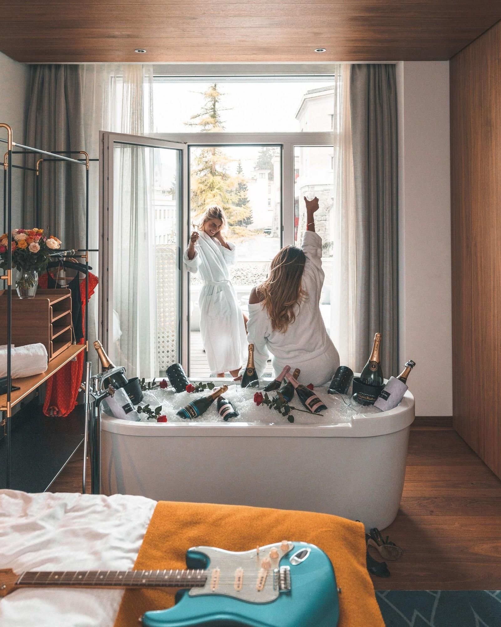 Ein Raum mit einer Badewanne, die mit Champagnerflaschen, einer Gitarre und einer Person in einem Bademantel gefüllt ist.