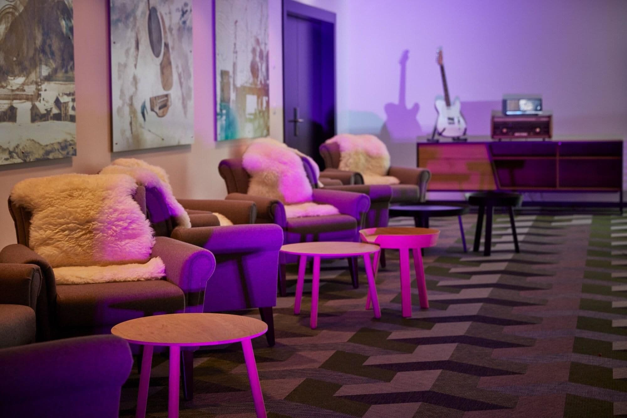 Una habitación con varios sofás y sillones, una alfombra estampada y una guitarra al fondo.