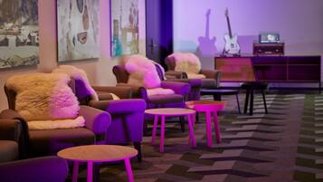 Una habitación con varios sofás y sillones, una alfombra estampada y una guitarra al fondo.