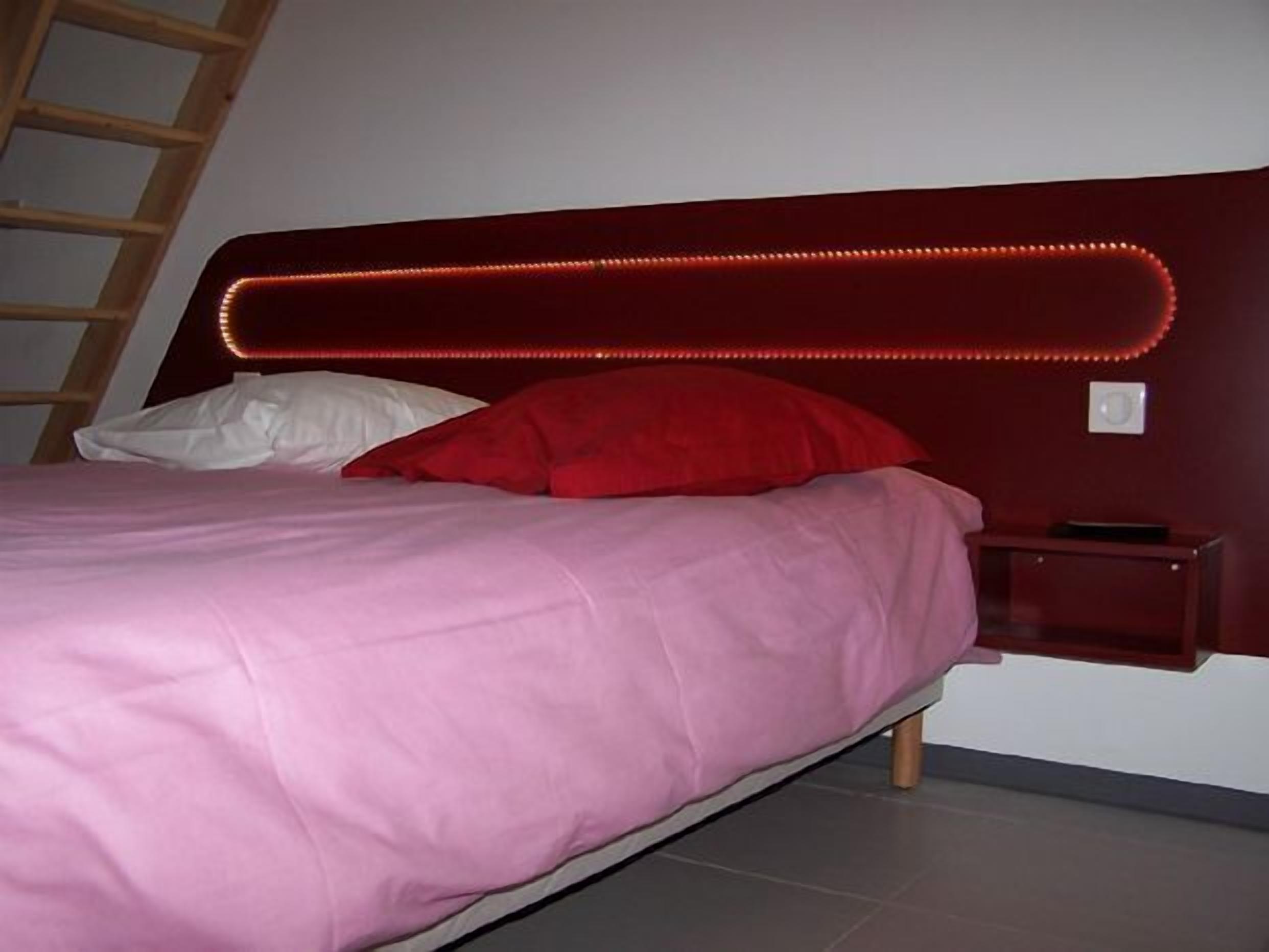 A bed with a headboard featuring LED lights, a red pillow, and a white pillow.