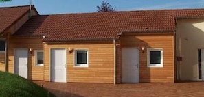 A row of wooden cabins with tiled roofs, each featuring a white door and a small window. - Hôtel Le Richevaux (Neufchateau)