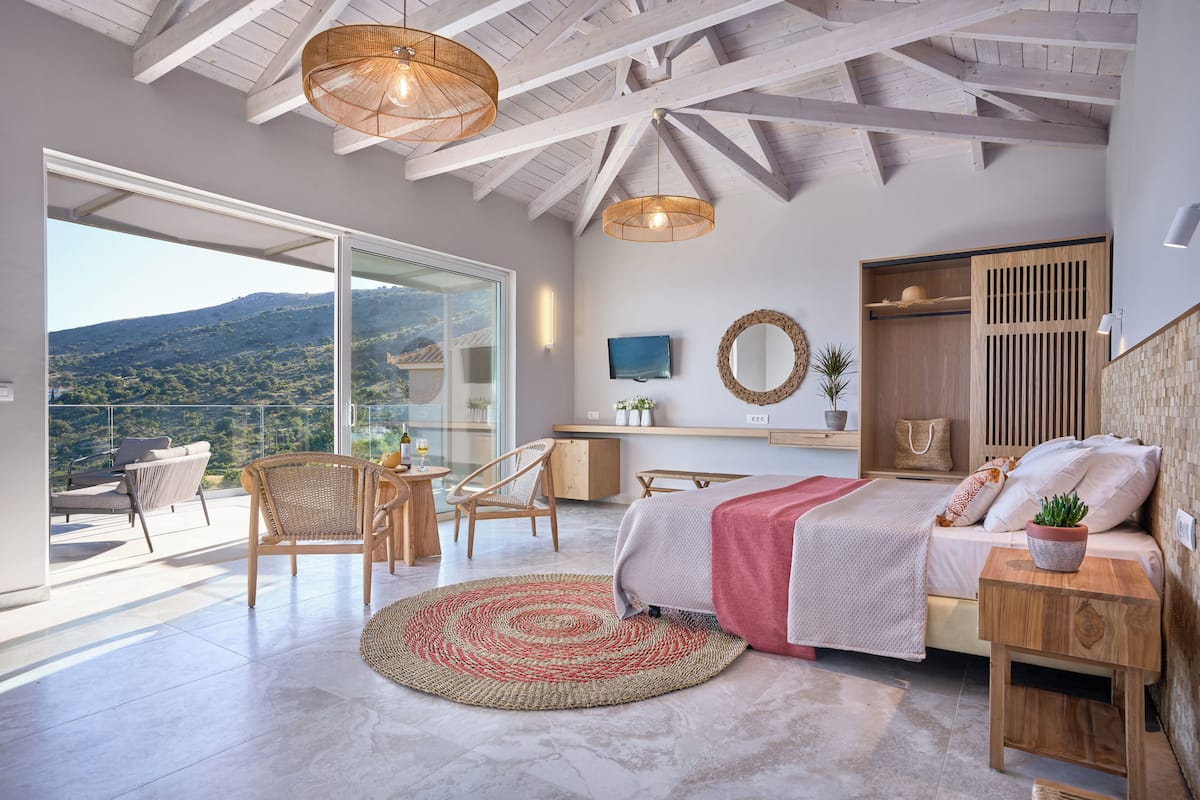 A bedroom with a bed, bedside table, and a view of a balcony with chairs and a table.