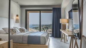 A modern hotel room with a large bed, a wooden desk, a TV, and a view of the sea. - Asteris Hotel (Kefalonia)