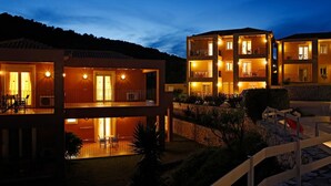 A modern hotel with multiple balconies, outdoor seating, and a stone retaining wall. - Asteris Hotel (Kefalonia)