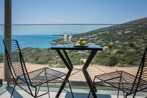 A balcony with a table, two chairs, and a view of the sea and hills. - Asteris Hotel (Kefalonia)