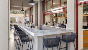 A bar area with a long counter, multiple bar stools, and a variety of bottles and glasses on shelves. - Asteris Hotel (Kefalonia)