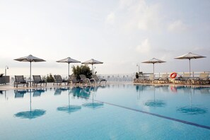 A swimming pool with lounge chairs and umbrellas, surrounded by a fence and a clear sky. - Asteris Hotel (Kefalonia)