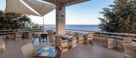 An outdoor dining area with wicker furniture and a view of the sea.