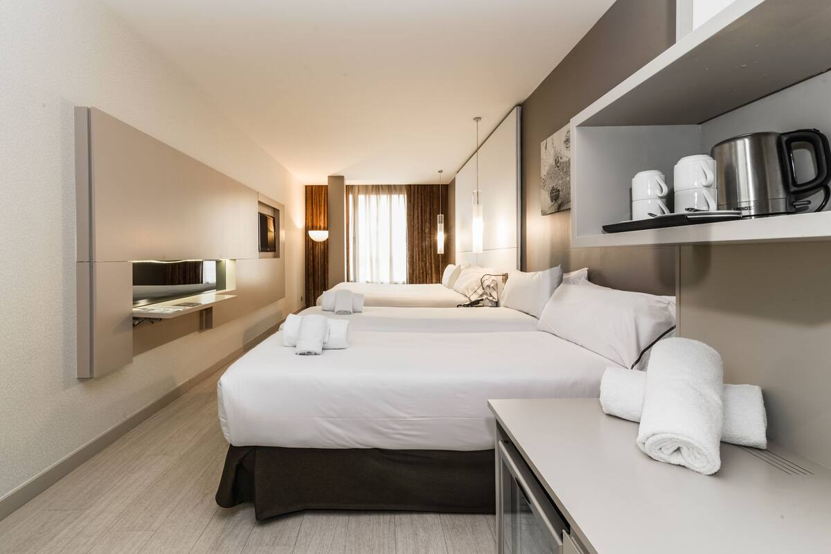 Habitación de hotel con dos camas, televisión, cafetera y tetera en la encimera.
