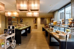 Ein Speisebereich eines Hotels mit mehreren Buffets, einem Weinkwagen und Blick auf die Stadt durch große Fenster.