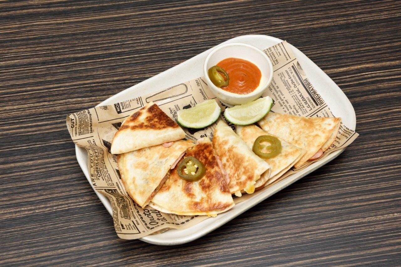 A plate of quesadillas with lime wedges and jalapeños, served on a newspaper-lined tray.