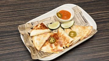 A plate of quesadillas with lime wedges and jalapeños, served on a newspaper-lined tray.