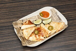A plate of quesadillas with lime wedges and jalapeños, served on a newspaper-lined tray.