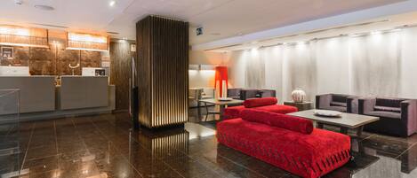 Eine moderne Lobby mit einer Rezeption, einer Sitzecke mit roten Sofas und einer Wandverkleidung.
